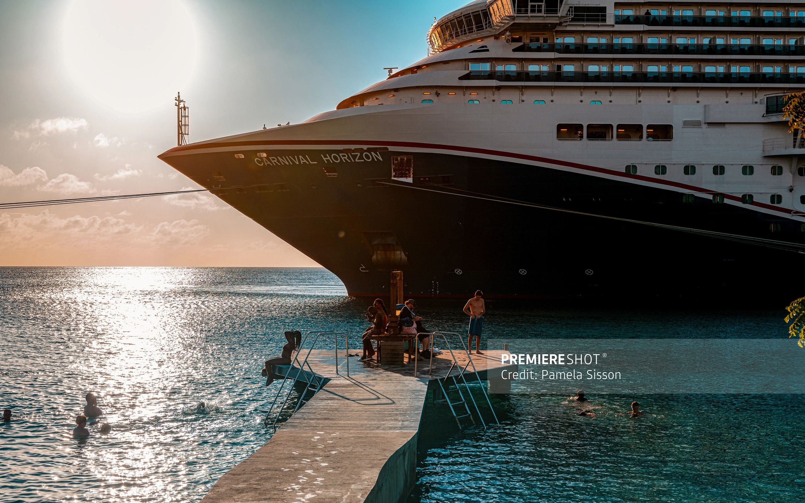 People enjoy swimming and relaxing near the Carnival Horizon cruise ship at sunset.