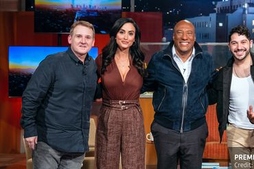 Five people posing together on a talk show set.