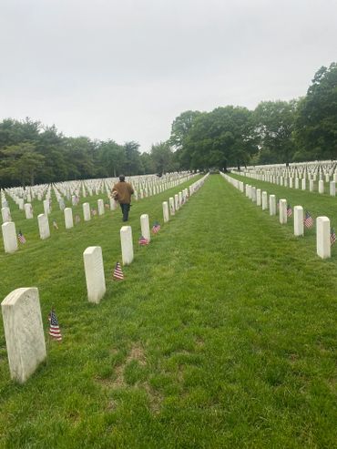 Rows of white gravestones with American flags in a peaceful cemetery.