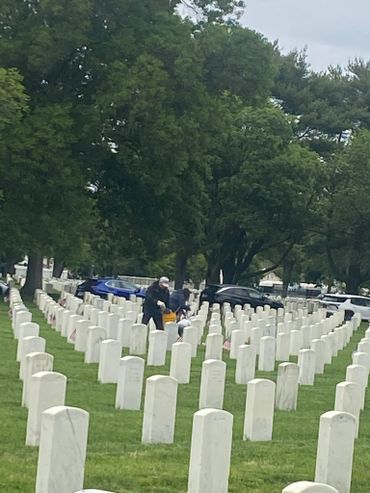 People walking among rows of white gravestones in a cemetery.