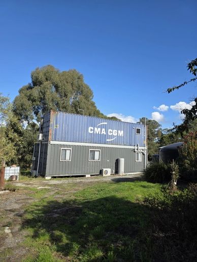Two stacked shipping containers converted into a building in a green outdoor area.