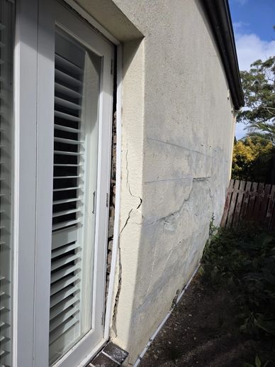 Cracked exterior wall near a white door with shutters.