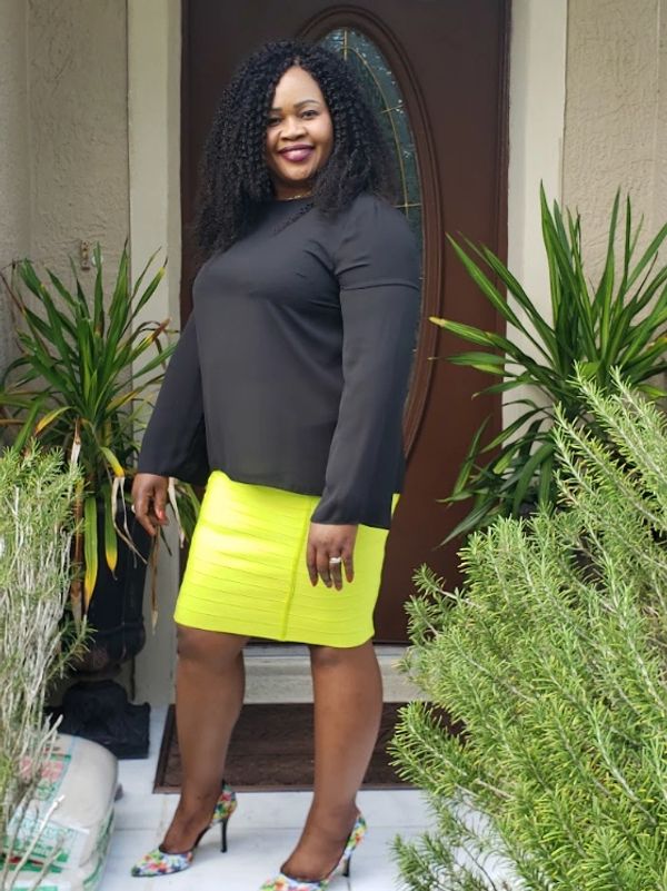 Woman posing outdoors in a bright yellow skirt and black top.