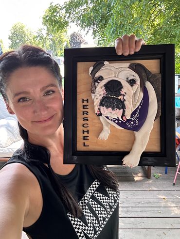 Woman holding a framed 3D portrait of a bulldog named Herschel.