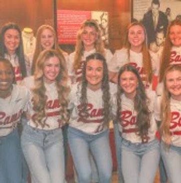 Group of young women in matching shirts posing and smiling indoors.
