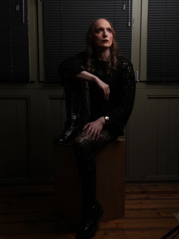 Person in dark clothing sitting on a box with contemplative expression.