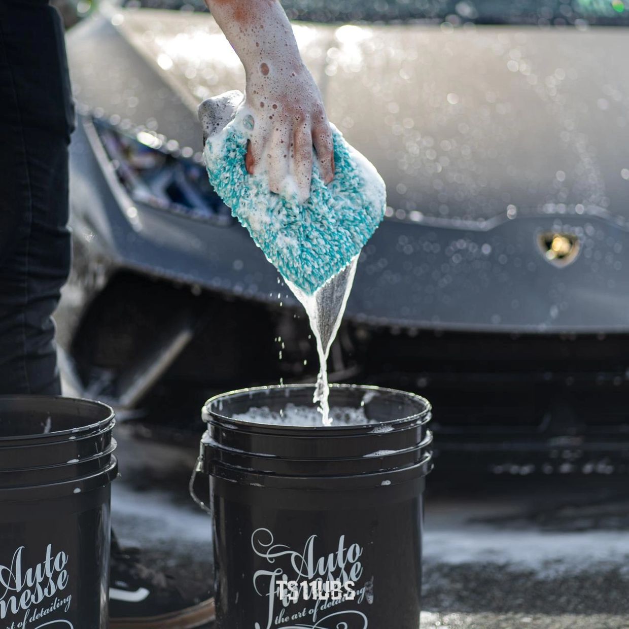Hand washing a luxury sports car with soapy mitt and bucket.