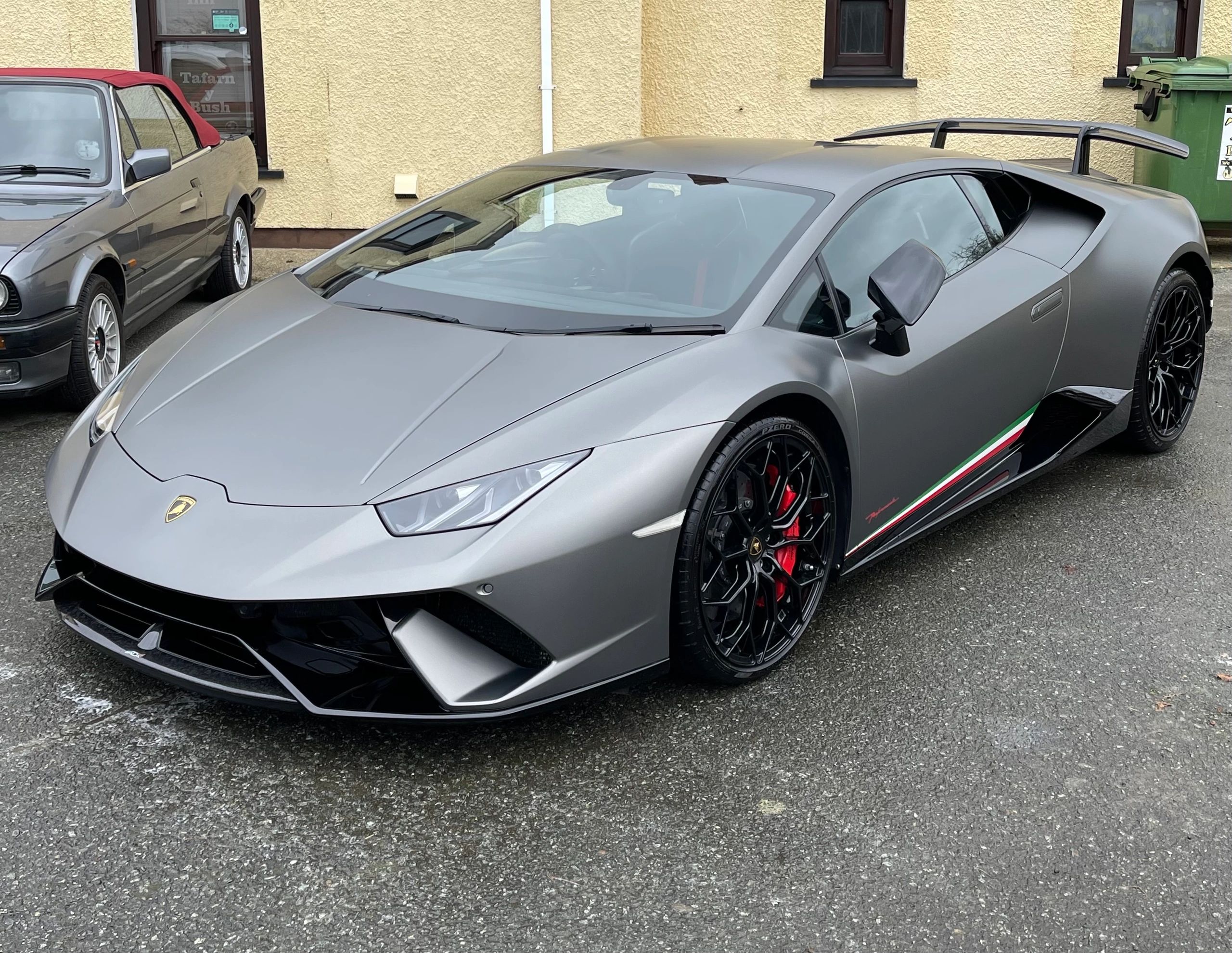 Matte grey Lamborghini Huracán with black rims parked on a wet street.
