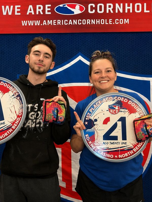 Two people posing with cornhole signs and bags, celebrating victory.