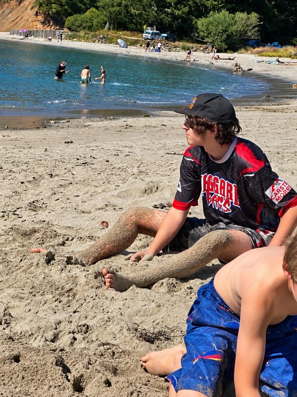 Teen sitting on sandy beach with legs covered in sand.