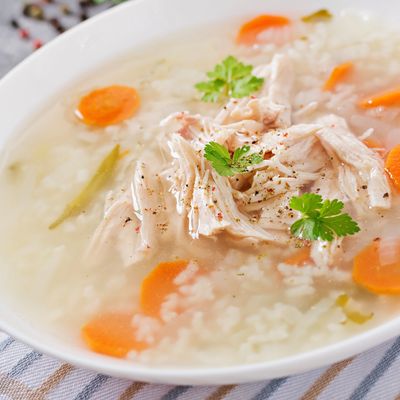 Bowl of chicken and rice soup garnished with herbs and sliced carrots.