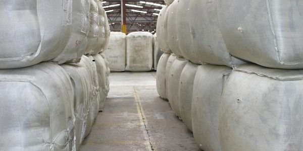 Rows of large, white fabric bales stacked in a warehouse aisle.