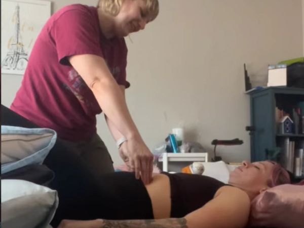 Person performing an abdominal massage on another person lying down.