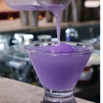 Pouring a vibrant purple drink into a glass.