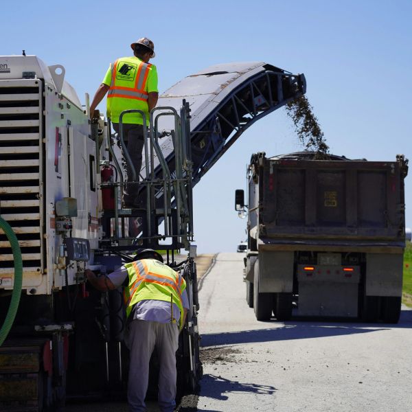 Road workers operating paving machinery on a highway.