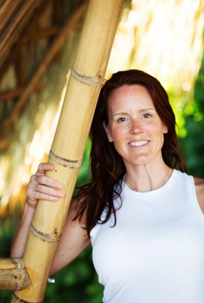 Smiling woman in a white tank top holding a bamboo pole outdoors.