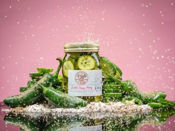 Jar of pickled cucumbers surrounded by fresh cucumbers and spices.