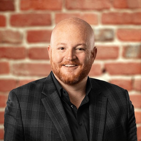 Smiling bald man with red beard in a checkered suit jacket.