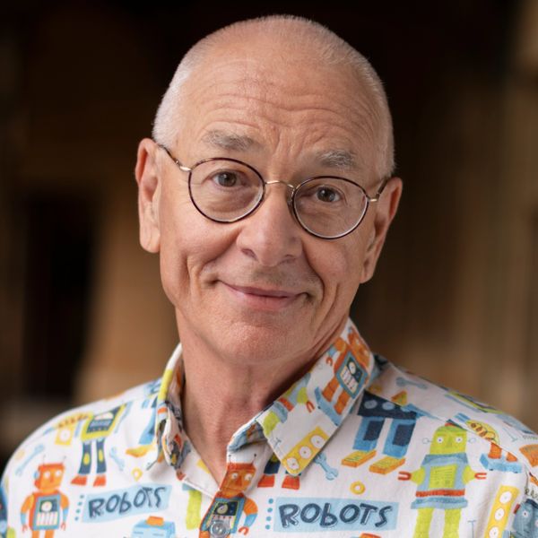 Smiling elderly man wearing glasses and a colorful robot-themed shirt.