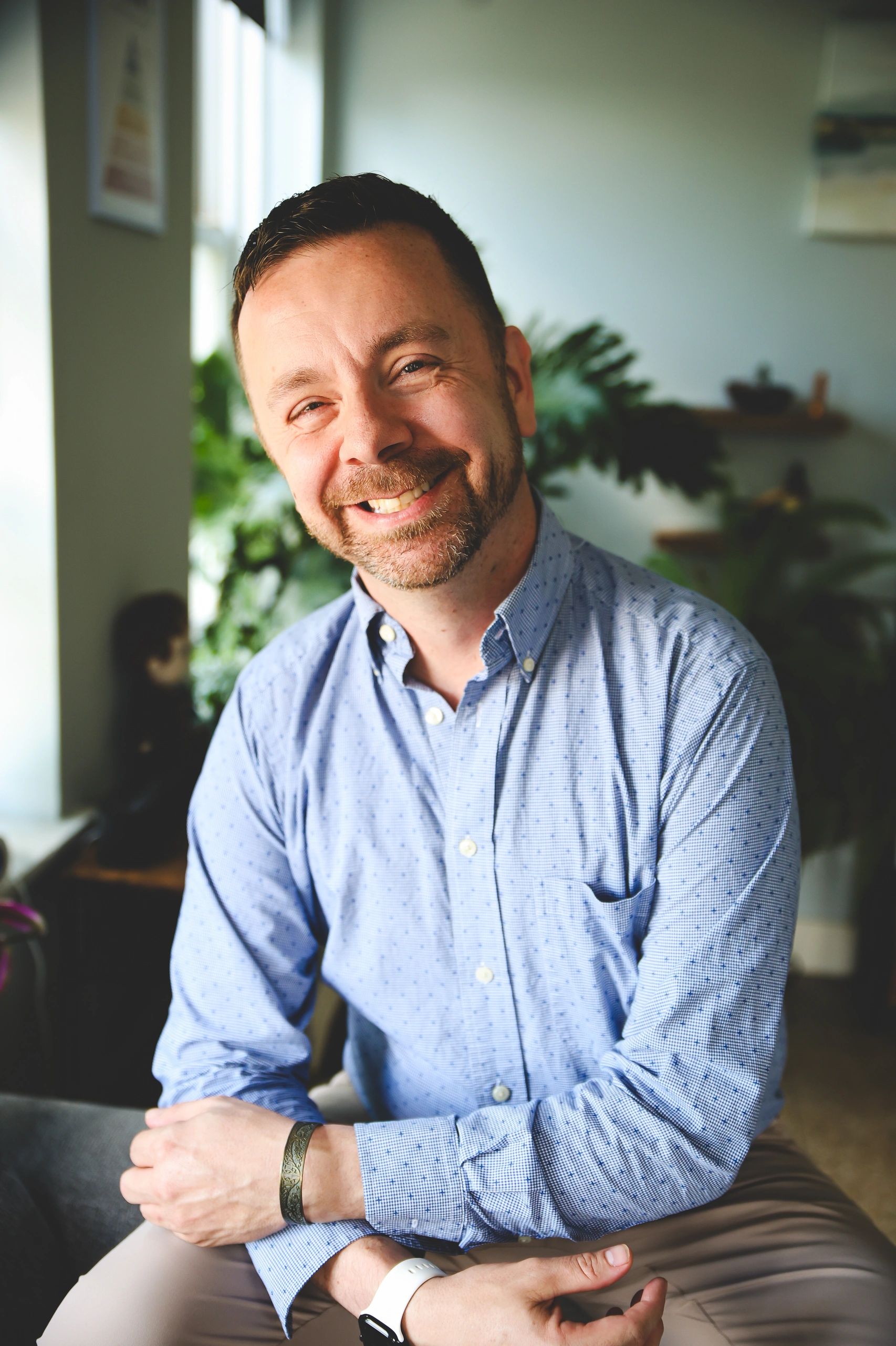 Smiling man in a blue shirt sitting comfortably indoors.