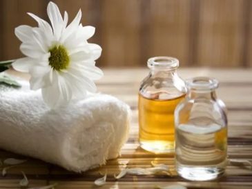 A white flower, towel, and two small bottles of oil on a wooden surface.