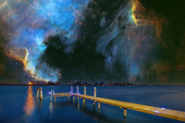Wooden pier extending into calm water under a vibrant starry sky.