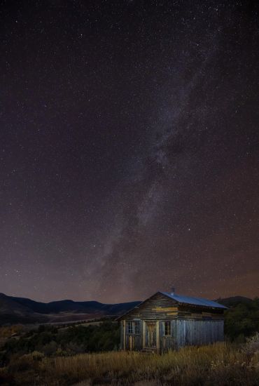 A rustic cabin under a star-filled night sky with the Milky Way visible.