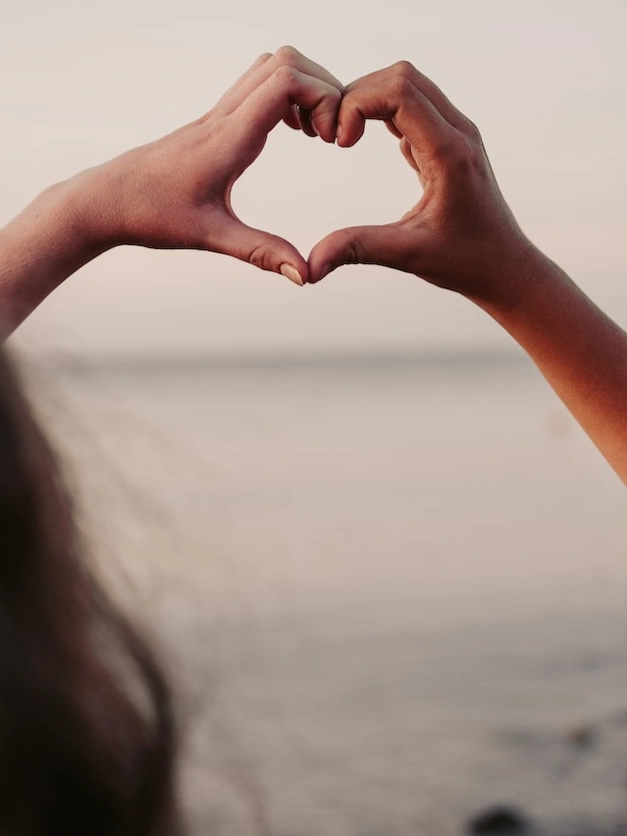 Two hands forming a heart with ocean in the background