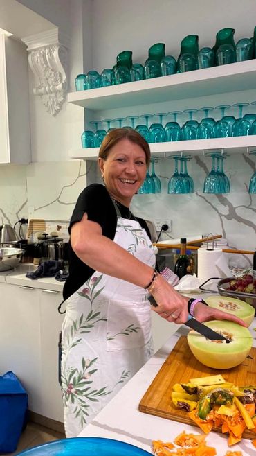 Smiling woman in a white apron cutting melon in a modern kitchen.