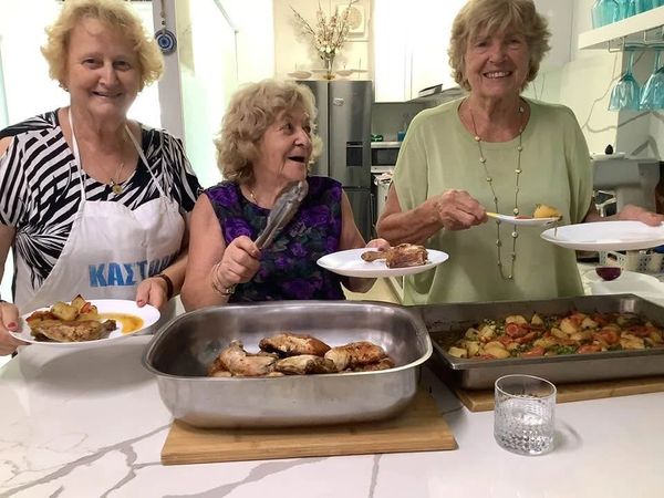 Three elderly women serving food in a kitchen, smiling happily.