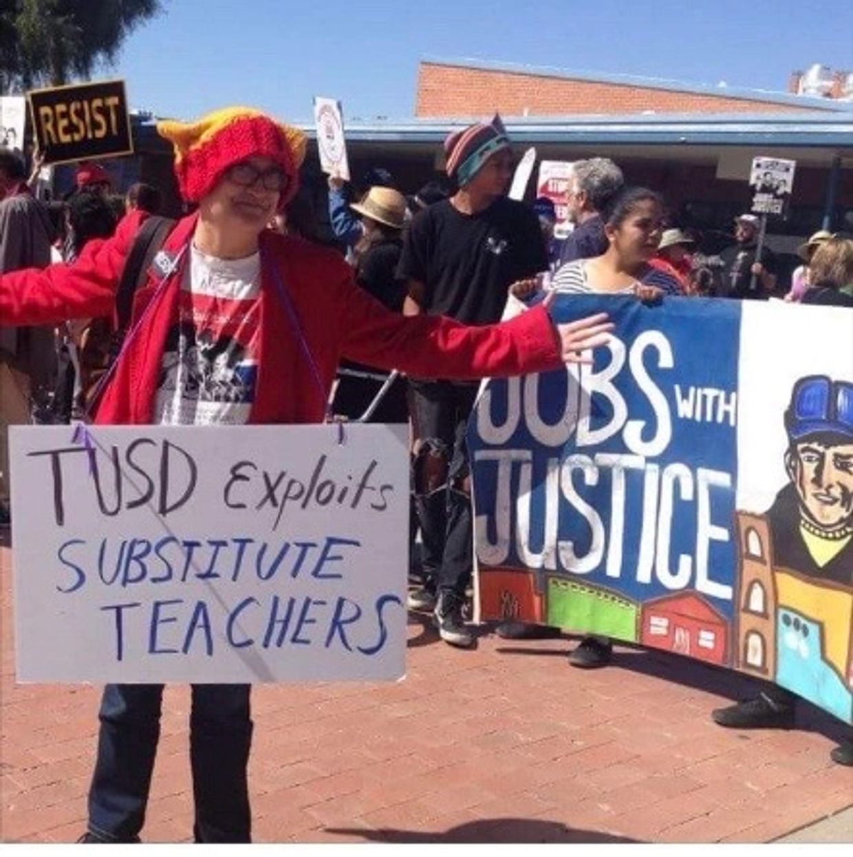 Protester holding sign against substitute teacher exploitation at rally.