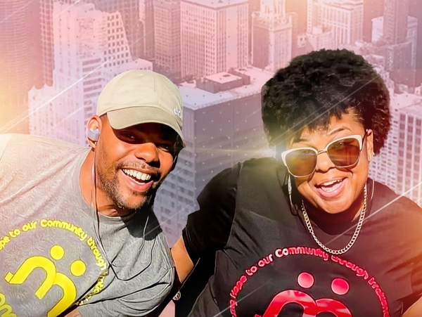 Two smiling people wearing matching community support t-shirts with cityscape background.
