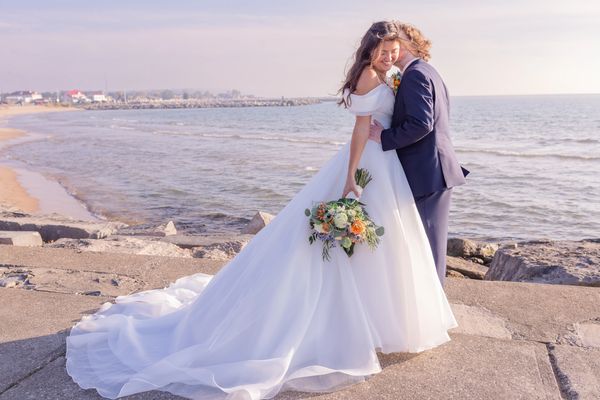 Bride and groom embrace by the seaside on their wedding day.