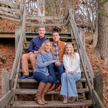 Family of four sitting on wooden stairs outdoors in fall.