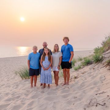 Family of five posing on a sandy beach at sunset.