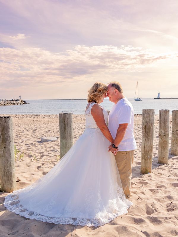 Couple in wedding attire sharing a tender moment on a sandy beach at sunset.