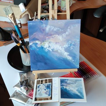 An artist's set-up with an oil painting, an easel, oil paints, sketchbook, colored markers, brushes