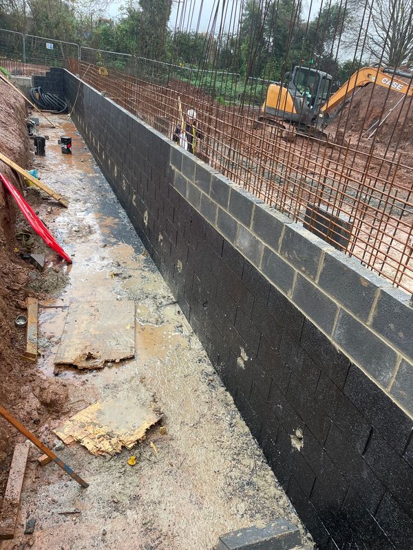 Construction site showing a newly built retaining wall with rebar framework and muddy ground.