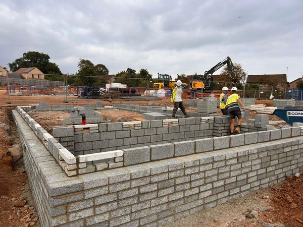 Workers building block walls on a construction site under a cloudy sky.