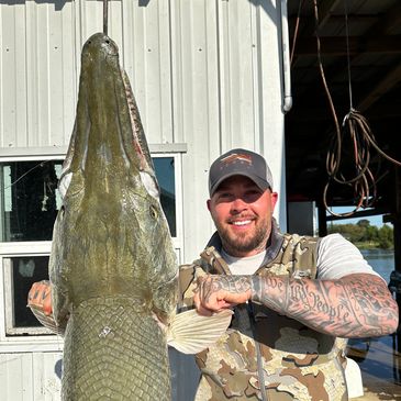 Man smiling standing next to a huge garfish.