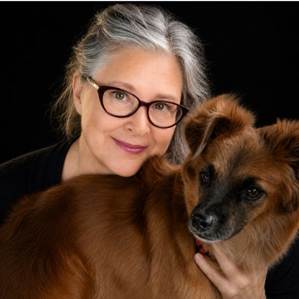 Smiling woman with glasses hugging a brown dog.