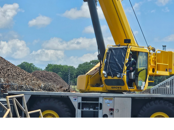 Yellow Grove crane operating near piles of scrap metal under a blue sky.