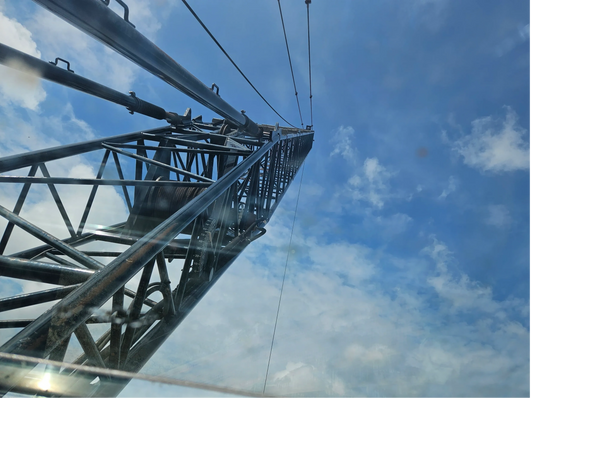Looking up at a tall metal tower against a blue sky with clouds.