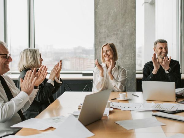 A group of people sit around the boardroom table, smiling and clapping, celebrating their results