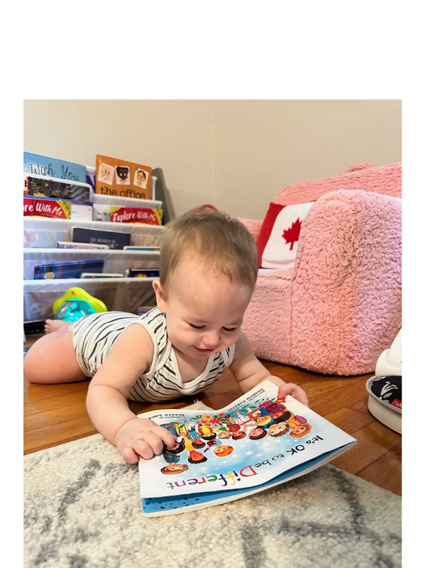 Baby smiling while looking at the book It’s OK to be Different.