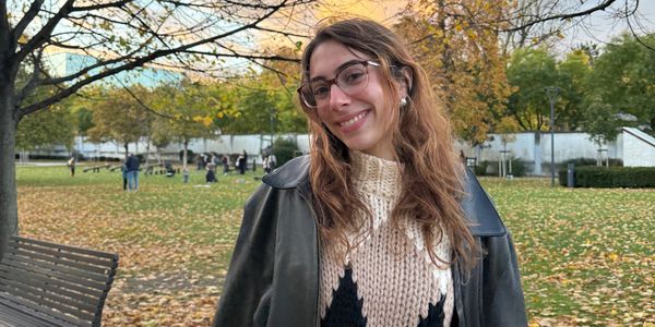 Young woman smiling in autumn park with glasses and leather jacket.