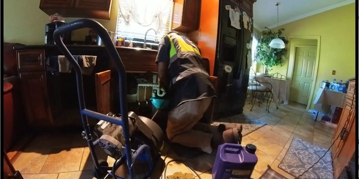 A plumber kneeling under a kitchen sink fixing pipes with tools around.