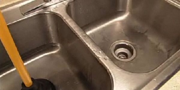 A double kitchen sink with a plunger inside one basin.