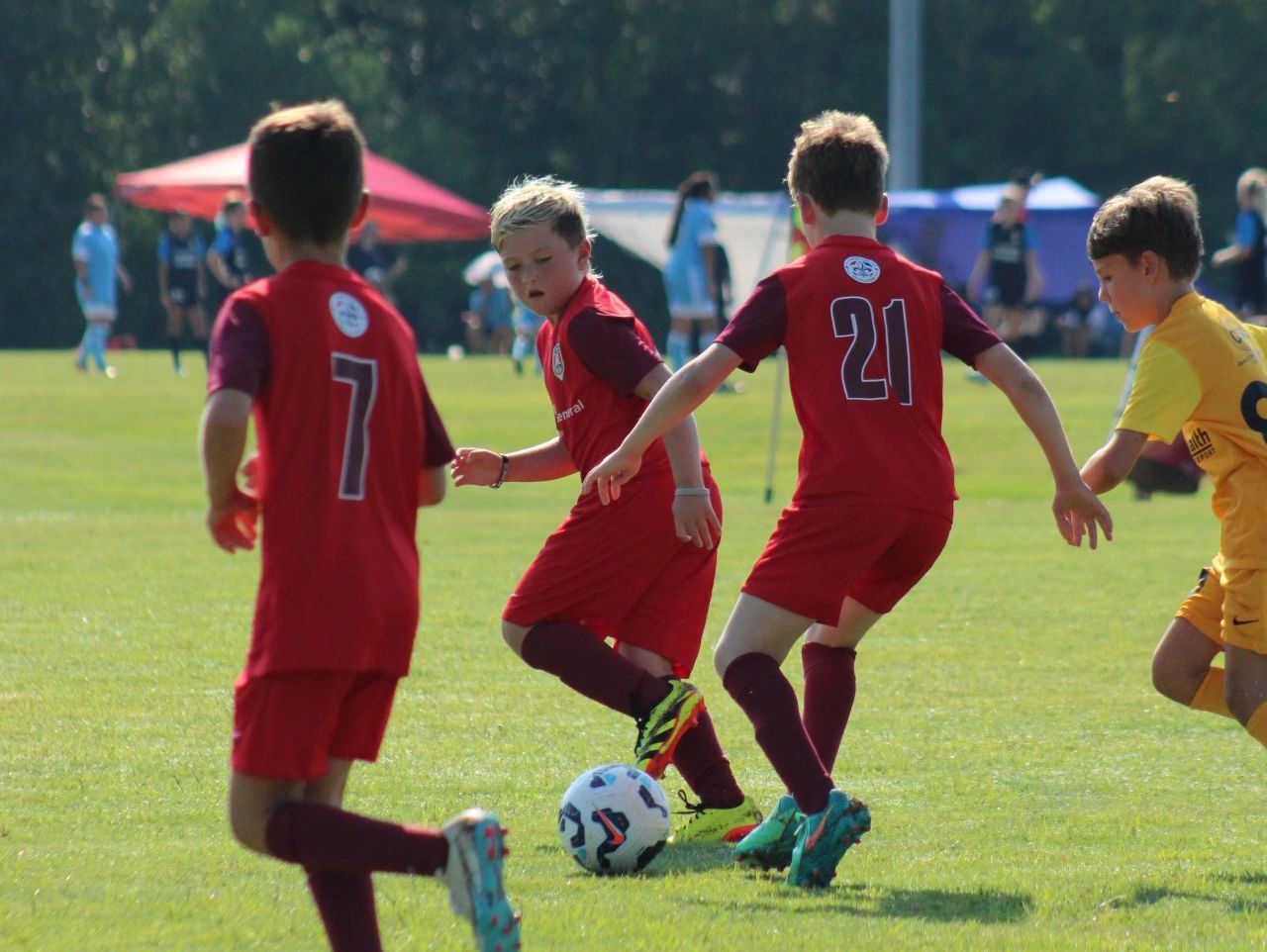 Young boys playing soccer on a sunny day in red and yellow uniforms.
