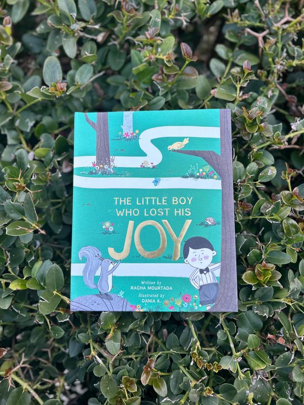 Children's book titled 'The Little Boy Who Lost His Joy' on green foliage.